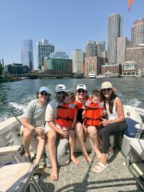 A joyful family enjoys a boat ride with a stunning city skyline in the background, all wearing life jackets for safety — a perfect day on the water.