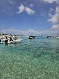 A lively scene at a popular swimming spot with boats anchored nearby, featuring a child enjoying the water with floaties — perfect for family fun and water activities.