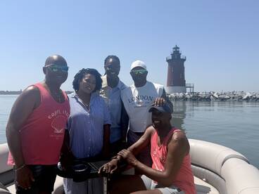 A cheerful group poses on a pontoon boat with a picturesque lighthouse in the background, capturing a memorable day on the water.
