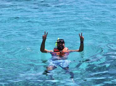 A snorkeler enjoys the vibrant turquoise waters, flashing a peace sign while floating — a perfect moment of fun and relaxation in the ocean.