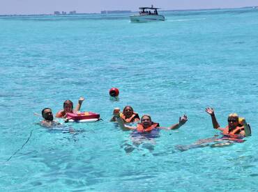 A lively group enjoys a refreshing swim in crystal-clear waters, celebrating with cocktails and laughter — the perfect backdrop for a fun day on the water.