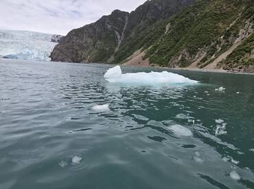 A stunning view of an iceberg floating in tranquil waters, with a backdrop of majestic glaciers and lush mountains, perfect for showcasing the beauty of nature.
