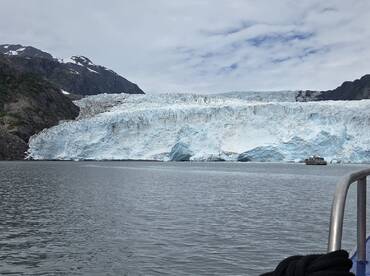 A stunning view of a massive glacier in Alaska, with a boat anchored nearby, showcasing the breathtaking natural beauty of the region.