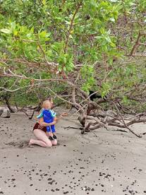 A mother and her child explore a sandy beach, surrounded by lush greenery — a perfect moment of family bonding in nature.