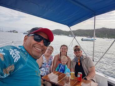 A joyful family enjoys their time on a boat, sharing drinks and smiles against a scenic backdrop of the water and surrounding hills.