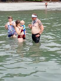 A family enjoys a fun day at the beach, wading in the water with drinks in hand — perfect for creating lasting memories during summer outings.