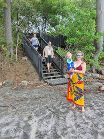 A joyful family descends the stairs from the beach, with a child in tow, capturing a moment of togetherness and adventure in a tropical setting.
