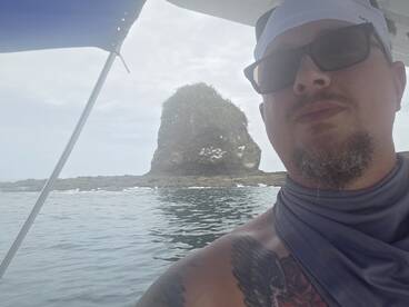 A man takes a selfie on a boat with a scenic rock formation in the background, capturing the essence of a memorable boating adventure.