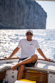 A man relaxes on the deck of a boat, enjoying the scenic ocean view near Capri — a perfect moment for sailing enthusiasts.