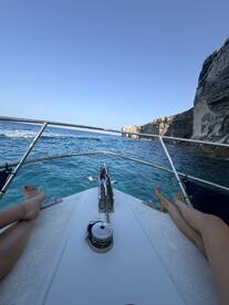 A relaxing moment on the bow of a boat, with feet resting over the edge, enjoying the stunning ocean view and cliffs in the background.