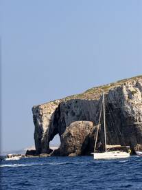 A picturesque sailboat navigates near a stunning coastal arch, showcasing the beauty of the landscape and the joy of sailing adventures.