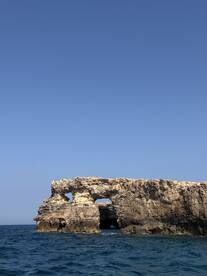 A stunning coastal rock formation stands majestically against a clear blue sky, perfect for scenic boat tours and exploration.