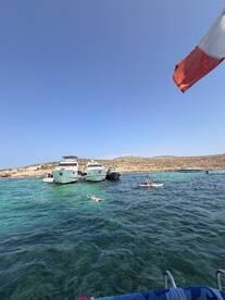 Guests enjoy a sunny day at a picturesque sandbar, with some swimming and others paddleboarding among anchored boats in crystal-clear waters.