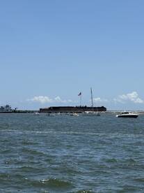 A scenic view of a harbor with various boats sailing near a historic fort, showcasing the beauty of a day on the water.