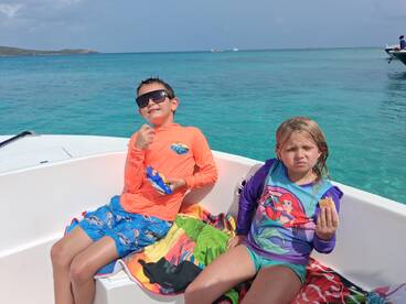 Two children enjoy snacks on a boat surrounded by beautiful turquoise waters, capturing a fun moment during their day on the water.