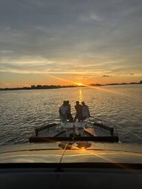 A group of friends poses on the bow of a boat during a stunning sunset, capturing a perfect moment of celebration on the water.