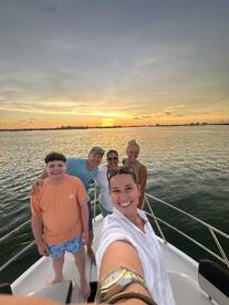 A joyful group captures a sunset selfie aboard a boat, celebrating together against a stunning backdrop of the setting sun — perfect for family outings and memorable moments on the water.
