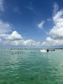 A lively scene of people swimming in clear turquoise waters, with boats anchored nearby — perfect for a fun day at the beach.
