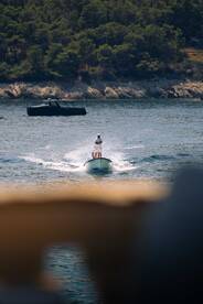 A person enjoys a thrilling ride on a small boat, creating a splash in the serene waters surrounded by lush greenery — a perfect snapshot of summer adventures on the water.