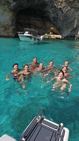 A joyful group of friends enjoys a refreshing swim in crystal-clear turquoise waters, with a boat anchored nearby, perfect for a fun day out on the water.