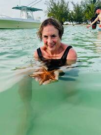 A woman joyfully holds a starfish while swimming in clear waters, showcasing a memorable wildlife interaction in a tropical paradise.