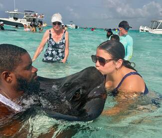 A thrilling encounter as a young girl kisses a stingray while a man observes nearby — a memorable wildlife experience in the crystal-clear waters.