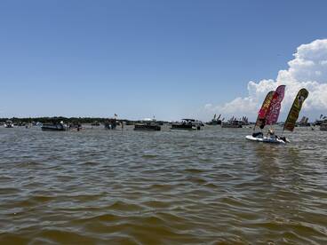 A vibrant scene of boats enjoying a sunny day on the water, featuring paddleboarding and festive flags, perfect for summer fun and gatherings.