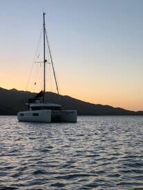 A serene view of a catamaran anchored at sunset, surrounded by tranquil waters and mountains, perfect for a peaceful evening on the water.