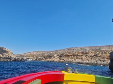 A vibrant view from the bow of a boat cruising along a stunning coastline, showcasing the natural beauty of the rocky landscape and clear blue waters.