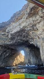 A scenic view of a boat navigating through a natural rock arch, showcasing the stunning coastline and adventure on the water.