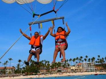 A couple enjoys an exhilarating parasailing experience over a beautiful beach, capturing the thrill of adventure in a tropical paradise.
