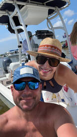 A cheerful couple takes a selfie on a boat under the sun, capturing a fun moment on the water.