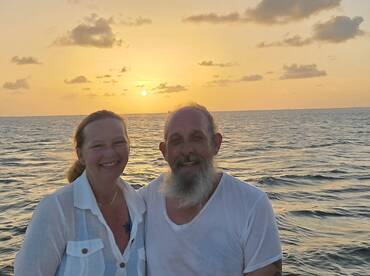 A couple smiles together against a stunning sunset backdrop, capturing a romantic moment on the water — perfect for anniversary celebrations or sunset cruises.
