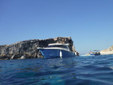 A beautiful blue boat is anchored near a rocky coastline, showcasing the serene waters and clear skies — perfect for a day of exploration.