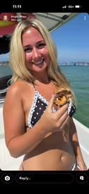A young woman enjoys a freshly shucked oyster while smiling on a boat under the sun — a perfect moment for seafood lovers on a sunny day out on the water.