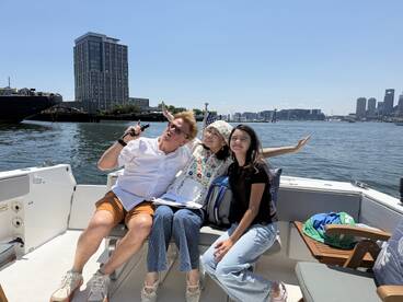 A joyful group poses for a photo on a boat, enjoying a sunny day with a vibrant cityscape in the background — perfect for memorable outings on the water.
