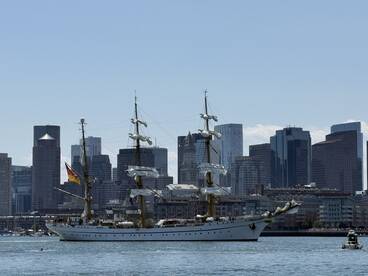 A majestic yacht sails through the harbor with a stunning city skyline in the background, showcasing the perfect blend of maritime elegance and urban beauty.