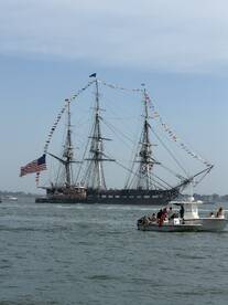 A historic sailing ship adorned with flags navigates the waters, with a group of people enjoying the view from a nearby boat — a perfect scene of maritime celebration.