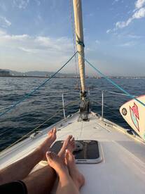 A couple enjoys a relaxing moment on the bow of a sailboat, with their feet visible against the backdrop of a serene ocean and distant shoreline — perfect for romantic sailing adventures.