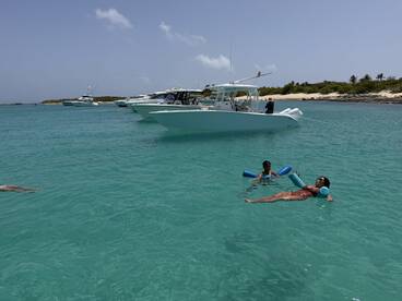 A family enjoys a sunny day at the beach, with a child playing in the water and an adult relaxing while floating — a perfect scene for summer fun and family bonding.