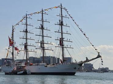 A majestic tall ship adorned with colorful flags sails through the harbor, showcasing its impressive rigging and crew. Perfect for maritime enthusiasts and sailing events.