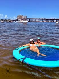 A couple enjoys a sunny day on a floating mat in the water, perfect for relaxation and fun under the sun.