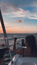 A couple enjoys a sunset cruise, toasting with cocktails while capturing the moment on their phones — a perfect blend of relaxation and celebration on the water.