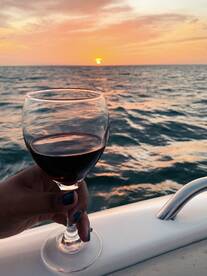 A hand holds a glass of red wine against a stunning sunset backdrop over the ocean, perfect for romantic evenings or sunset cruises.