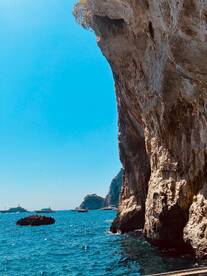 A stunning view of rocky cliffs and multiple boats anchored in the vibrant blue ocean, showcasing the natural beauty of the coastline.