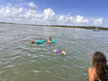 A man relaxes on a floating mat while enjoying the water, accompanied by a dog in a life jacket. This scene captures the essence of leisure and fun in the sun.