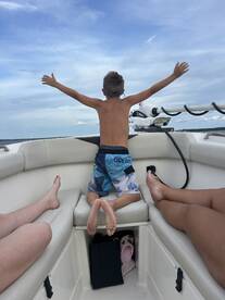 A joyful child spreads his arms wide on a boat, embracing the thrill of the ride — a perfect moment of fun and freedom on the water.