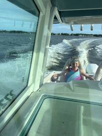 A young girl enjoys a fun day on the water, steering a boat with a big smile — perfect for family adventures and creating lasting memories.