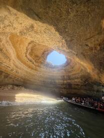 A group of tourists enjoys a boat ride through a stunning cave, illuminated by sunlight filtering through the opening above — a breathtaking adventure in nature.