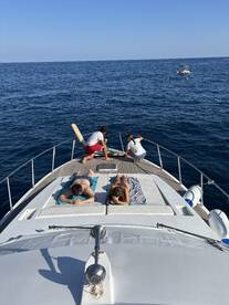 A group enjoys a relaxing day on a yacht, sunbathing on the deck while surrounded by the serene blue waters — perfect for a summer getaway.